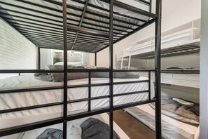 A bunk bed room with a metal frame, white bedding, and a window providing natural light.