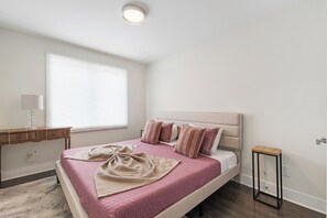 Un dormitorio con cama, mesita de noche, lámpara y ventana.