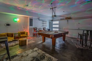 Une pièce équipée d’une table de billard, de canapés jaunes, d’un projecteur et d’un plafond sur lequel sont projetées des lumières.