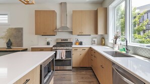 A modern kitchen with wooden cabinets, stainless steel appliances, and a large window providing a view of the outdoors. - 19 Bed Home Near Downtown with Game room (Nashville)