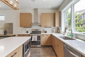 A modern kitchen with wooden cabinets, stainless steel appliances, and a large window providing a view of the outdoors. - 19 Bed Home Near Downtown with Game room (Nashville)