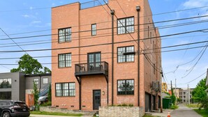 A multi-story brick building with a balcony on the second floor, a visible garage door, and a parked SUV. - 19 Bed Downtown Rooftop Gameroom Walk To Broadway (Nashville)