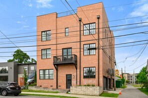 A multi-story brick building with a balcony on the second floor, a visible garage door, and a parked SUV.
