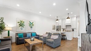 Un salon moderne avec un canapé, des fauteuils, une table basse et une cuisine en arrière-plan.