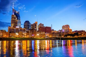 A city skyline at dusk with illuminated buildings reflecting on a body of water.