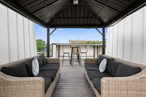 A covered outdoor seating area with two wicker sofas and a table, a clear view of the sky, and a building in the background. - 19 Bed Downtown Rooftop Gameroom Walk To Broadway (Nashville)