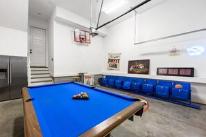 A pool table with balls, a projector, and a digital scoreboard in a room with blue chairs and a refrigerator.