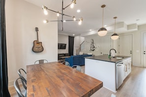 A modern kitchen with a wooden dining table, pendant lights, and a built-in island with a sink. - 21 Bed Near Downtown Rooftop & Pool Table (Nashville)