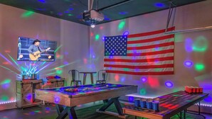 A room with a pool table, a projector screen displaying a guitar player, and an American flag.