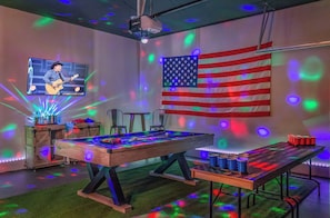 Une pièce avec une table de billard, un écran de projection sur lequel on peut voir un guitariste, et un drapeau américain.