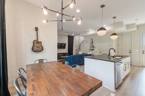 Une cuisine moderne dotée d’un îlot central, de luminaires suspendus et d’un coin repas avec une table en bois.