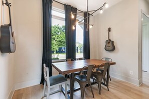 Uma sala de jantar com uma mesa e cadeiras de madeira, um violão na parede e uma janela com cortinas.