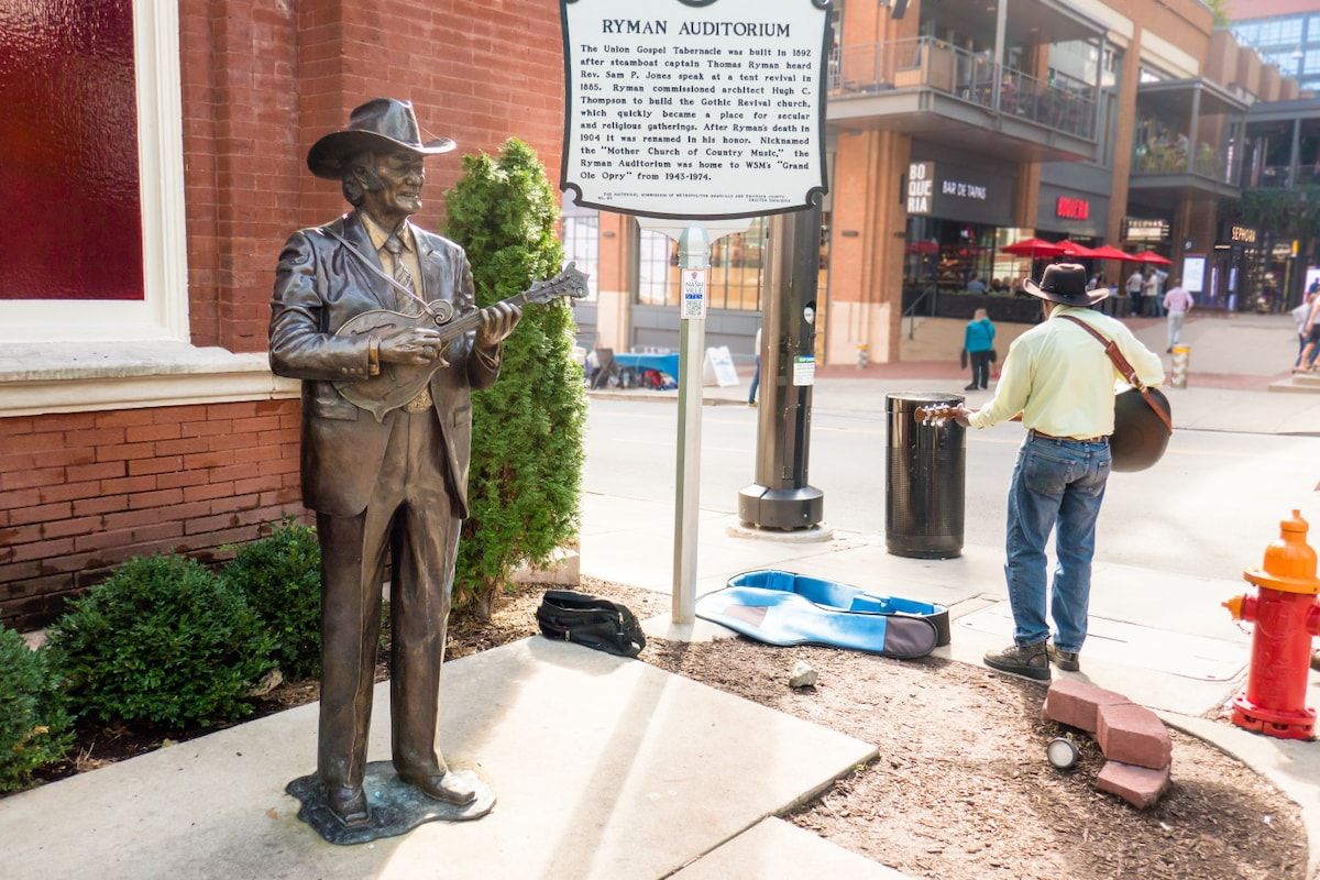 A statue of a man with a guitar, a sign with historical information, and a red fire hydrant.