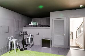 Una habitación compacta con una litera, una pequeña mesa con sillas, una puerta para mascotas y una escalera que sube a un nivel superior.