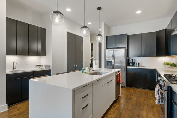 Una cocina moderna con una isla central, muebles oscuros, electrodomésticos de acero inoxidable e iluminación colgante.