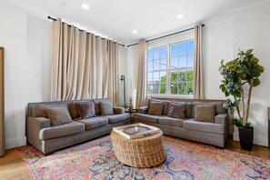A living room with a sectional sofa, a round coffee table, and a large window with curtains.
