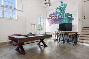 A pool table in a room with a large mural, a television, and a bar area.