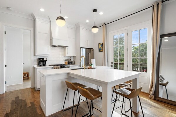 A modern kitchen with white cabinetry, a central island with stools, and pendant lighting. - 18 Bed Downtown View Walk To Broadway (Nashville)