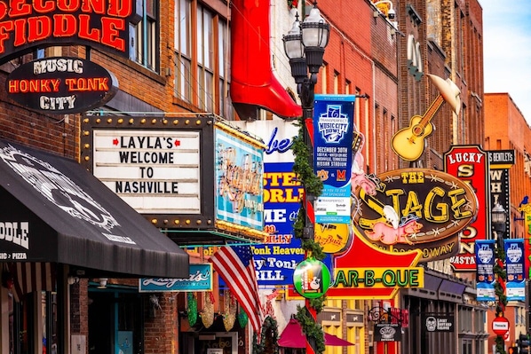 Een levendig straatbeeld met diverse borden, waaronder een bord met de tekst 'Music Honky Tonk City' en een bord met 'Layla's Welcome to Nashville'.