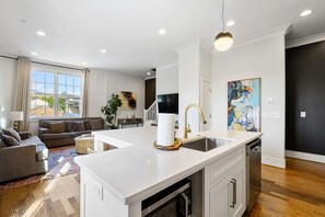 A modern kitchen with a white countertop, a sink, and a dishwasher. There is a dining area with a white table and chairs, and a living room with a sofa and a coffee table. - 18 Bed Downtown View Walk To Broadway (Nashville)