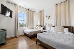 A hotel room with two beds, a TV, a window with curtains, and a wall-mounted bull skull decoration.
