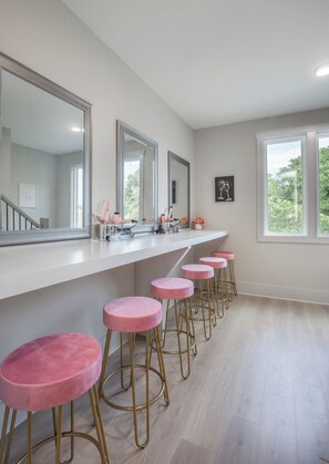 A kitchen with a long counter, pink stools, and a large mirror.