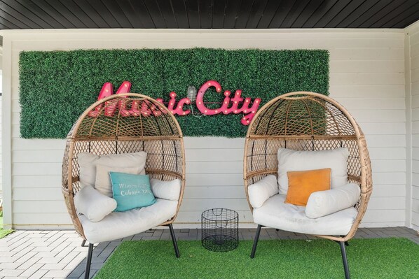 Two wicker chairs with cushions, a green artificial grass floor, and a wall with a sign reading 'Music City'.
