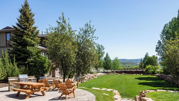 Un patio con muebles de madera, una parrilla de piedra y un césped cuidado.