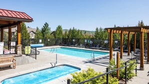 Una piscina con sillas de descanso y un pabellón, rodeada por una valla y árboles.