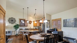 Una cocina moderna con armarios de madera, una isla central, iluminación colgante y un comedor con una mesa redonda y sillas.