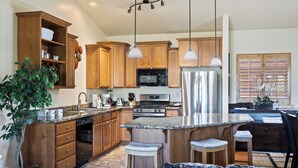 Una cocina moderna con armarios de madera, electrodomésticos de acero inoxidable, encimeras de granito, iluminación colgante y una isla central con taburetes de bar.