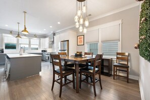 A modern kitchen with a central island, wooden chairs, pendant lighting, and a view of the outdoors.