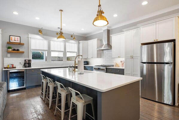 A modern kitchen with a central island, bar stools, stainless steel appliances, and pendant lighting.