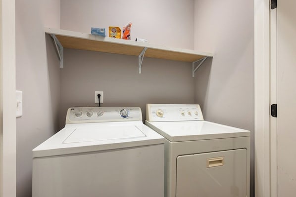 A laundry room with two washing machines and a shelf above.