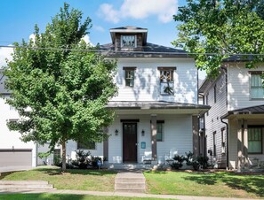 A two-story house with a front porch, a garage, and a large tree in the yard.