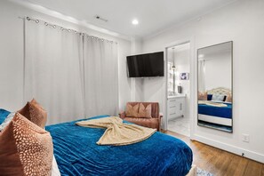 Een slaapkamer met een bed, een stoel, een televisie en een spiegel.