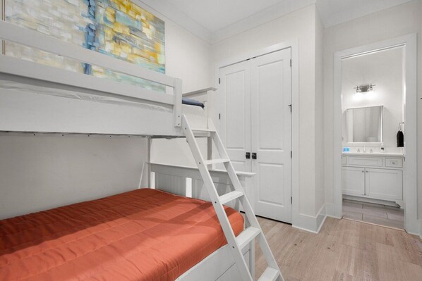 A bunk bed with a ladder, a white door, and a bathroom with a mirror.