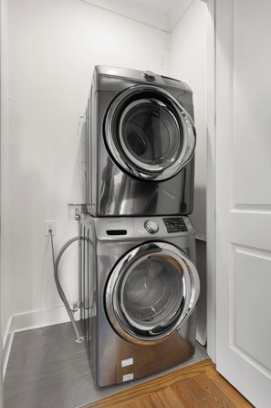A stacked washer and dryer unit in a corner with a visible power outlet and a hose.