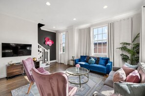 A living room with a blue sofa, a pink armchair, a coffee table, and a TV mounted on the wall.