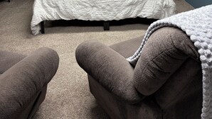 Une chambre à coucher comprenant un lit, deux tables de chevet, une commode, une fenêtre avec un rideau et une étagère fixée au mur.
