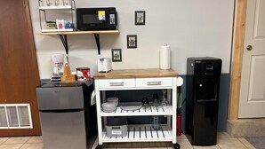 Une petite cuisine équipée comprenant un réfrigérateur, un four à micro-ondes, une machine à café et un petit chariot muni d’étagères de rangement.