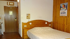 A bedroom with a wooden bed, a wooden door, a telephone, and a poster on the wall.