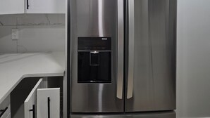 A stainless steel refrigerator with a water dispenser, white cabinets, and a marble backsplash.