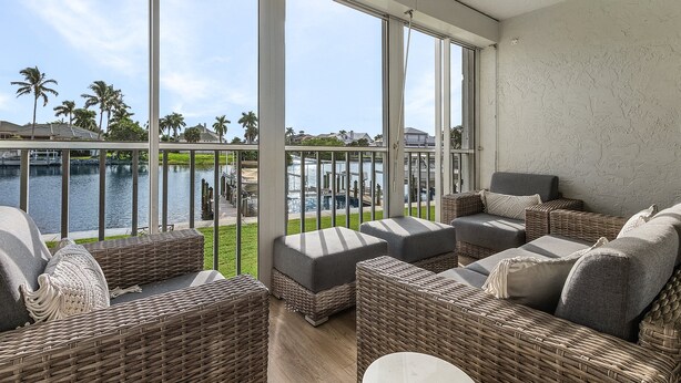 Een balkon met rieten meubilair, uitzicht op een wateroppervlak en een gazon.