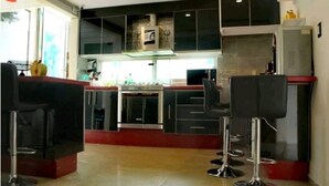 Una cocina moderna con armarios negros, electrodomésticos de acero inoxidable y una encimera roja. Hay dos taburetes negros en primer plano.