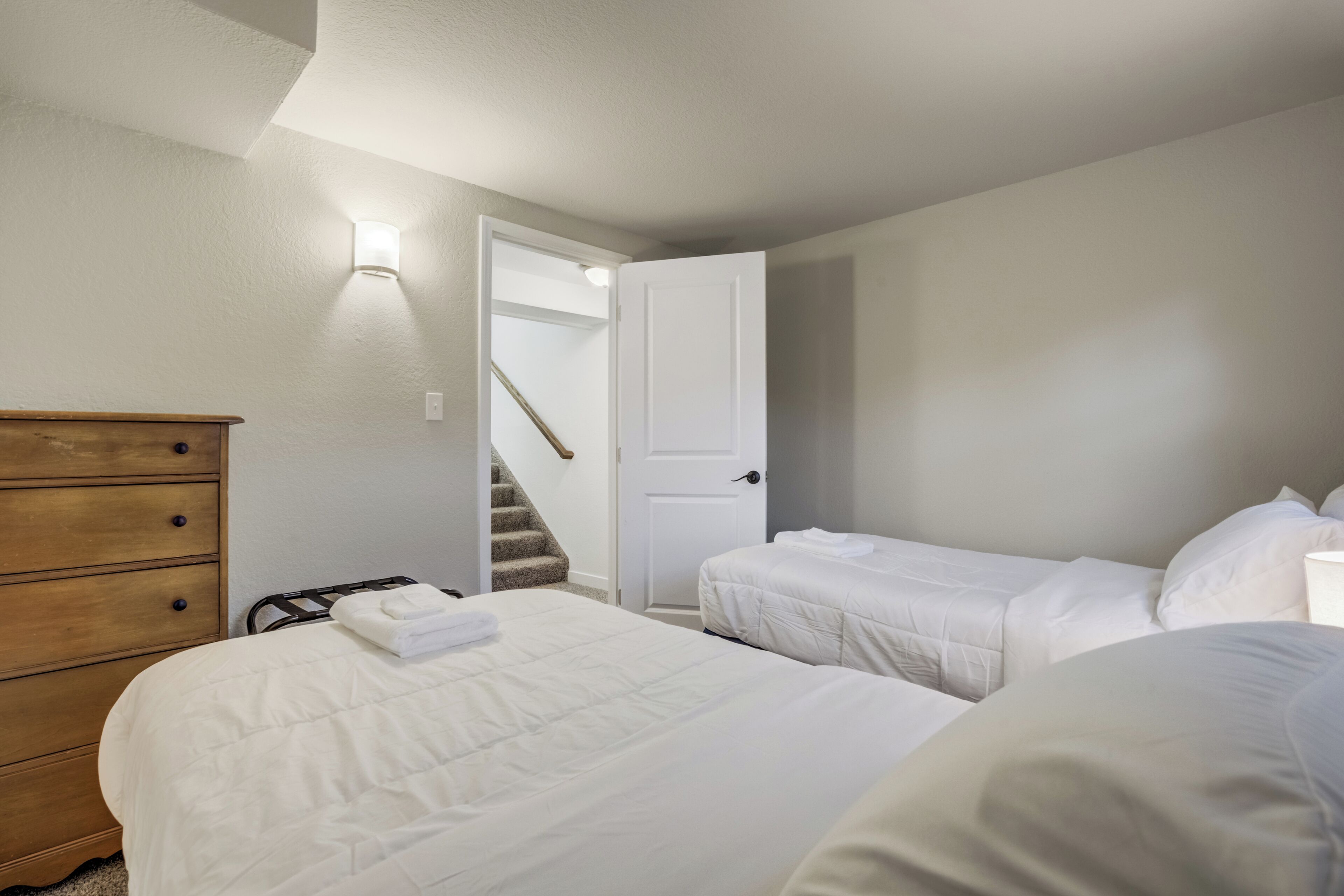 A bedroom with two beds, a wooden dresser, and a staircase leading to another room.