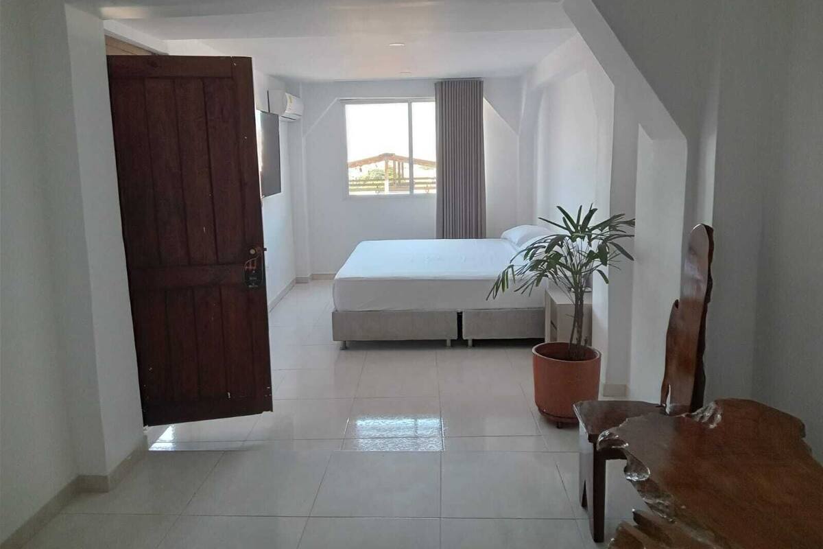 Ein Schlafzimmer mit einem Bett, einer Zimmerpflanze, einem Holzstuhl und einem großen Fenster.