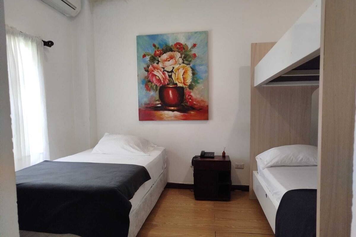 Ein kleiner, sauberer Raum mit zwei Einzelbetten, einem Blumenbild an der Wand und einem Holzboden.