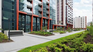 A modern building with multiple floors, large windows, and a landscaped area with grass and shrubs.