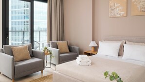 A modern hotel room with a large bed, two armchairs, a small table with a lamp, and a view of a cityscape through the window. - Towarowa Towers 106 Superior Studio (Warszawa)